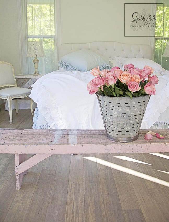 romantic room designs - peach and pink roses in a silver tin garden bucket sit on a pink vintage bench complement the white bed linens