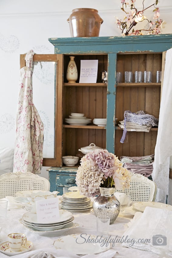 A beautiful shabby chic style tablescape with white china and linens and a distressed blue china cabinet - both from Shabby Chic Couture.