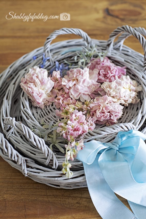 Three grey wicker trays sit inside one another, topped off with light pink peony flowers and tied together with a robin egg blue ribbon. This simple DIY floral peony wreath project is so easy to make!
