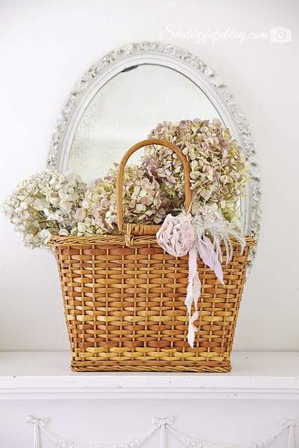 A vintage wicker basket with pastel Peony flowers in front of a white rimmed mirror - a beautiful and simple floral peony wreath display.
