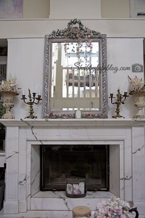 A French farmhouse style mantel display; marble fireplace, brass candelabras and an intricate white wood mirror with a stunning hand-carved wooden frame.