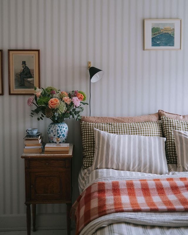 English country cottage styled bedroom with striped wallpaper as a backdrop and flowers next to the bed