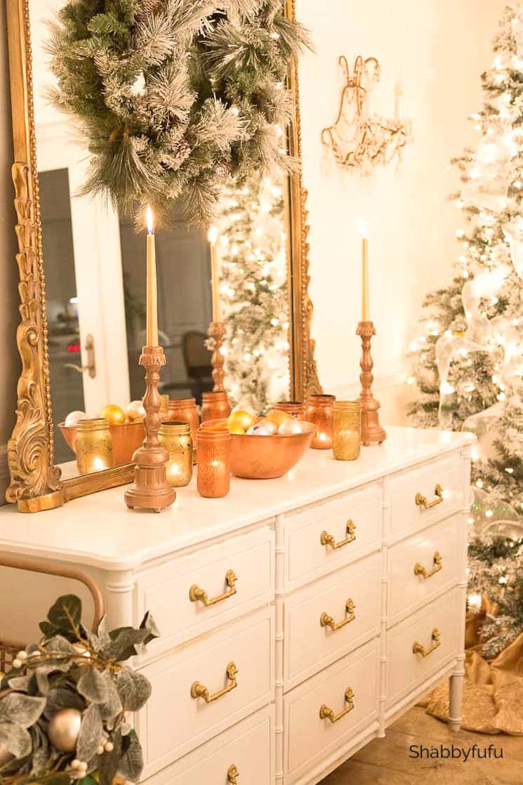 A room filled with gold and Christmas decor. There is lighted candles on the ornate dresser.