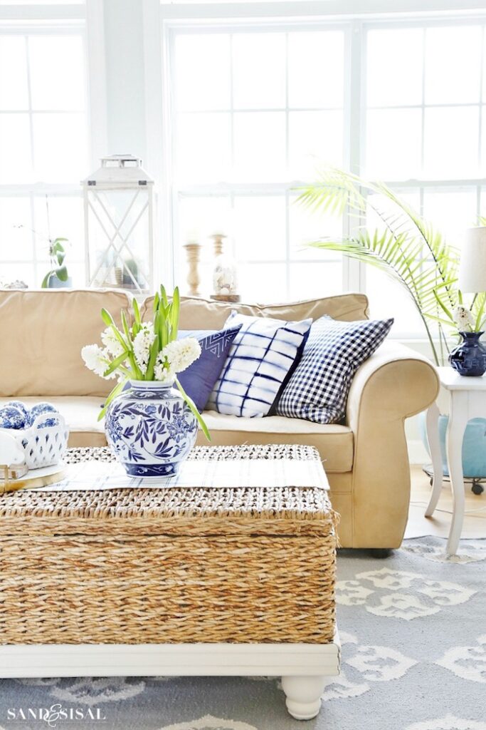Coastal inspired living room featuring wicker rattan coffee table, light tan sofa and blue pillows 