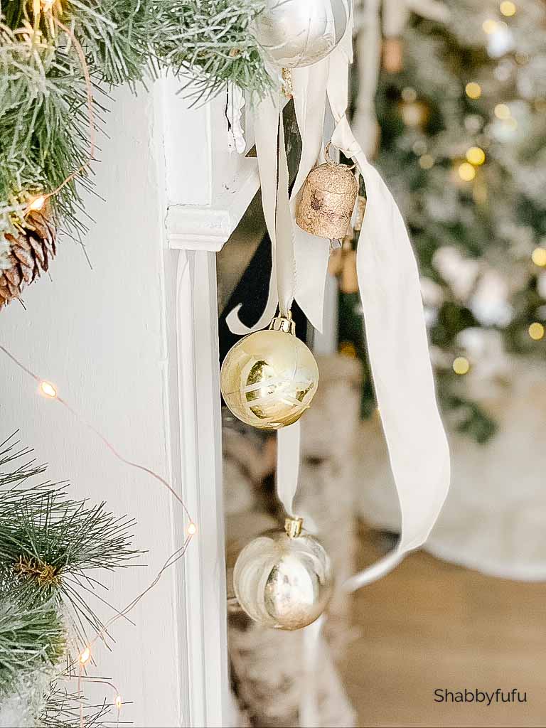 gold Christmas ornaments hanging from white ribbon on a mantel