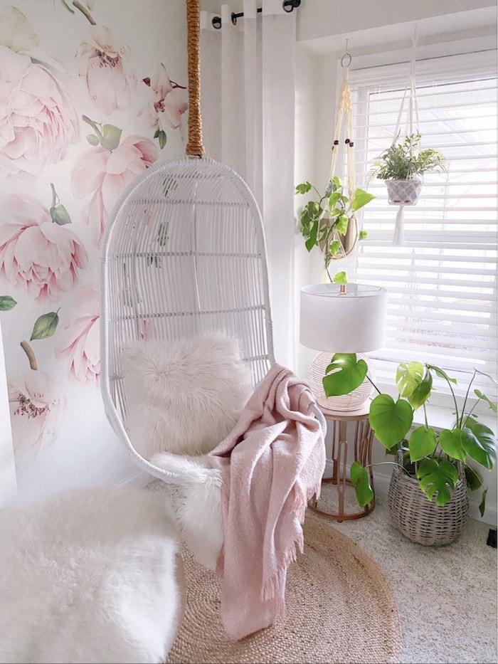 white hanging chair in the corner of a room with a wall behind it with large pink roses