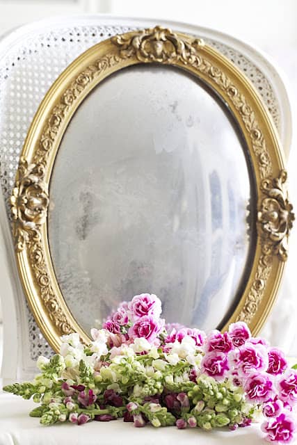 gold oval shaped ornate mirror with bunch of pink and white flowers lying in front