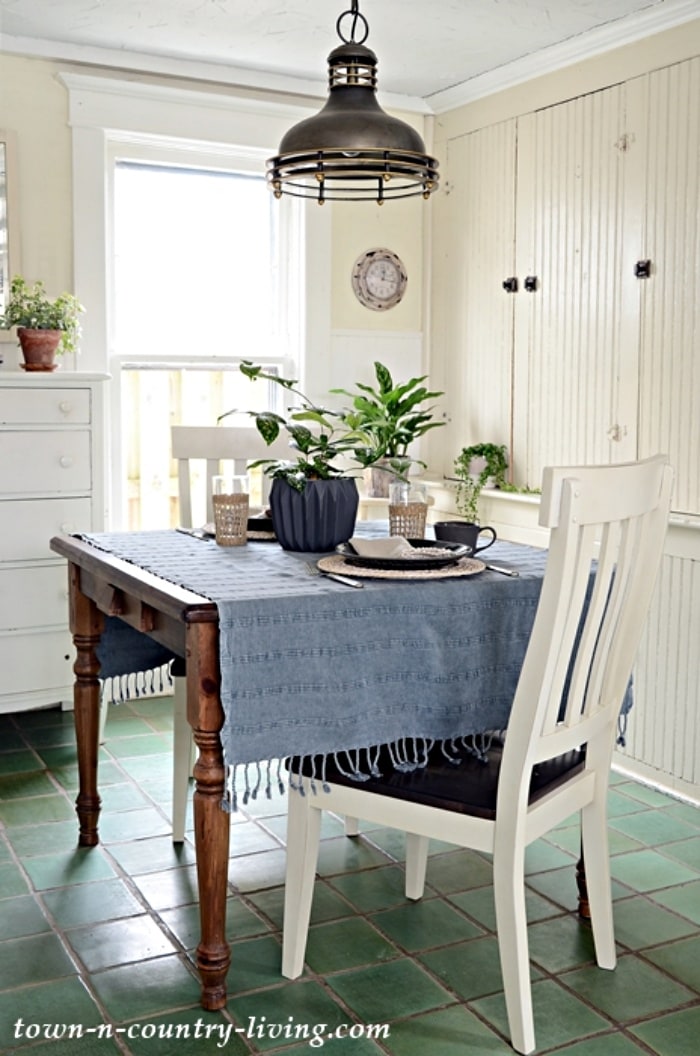 small square dining table with a blue table cloth, white chairs in front of white cabinets