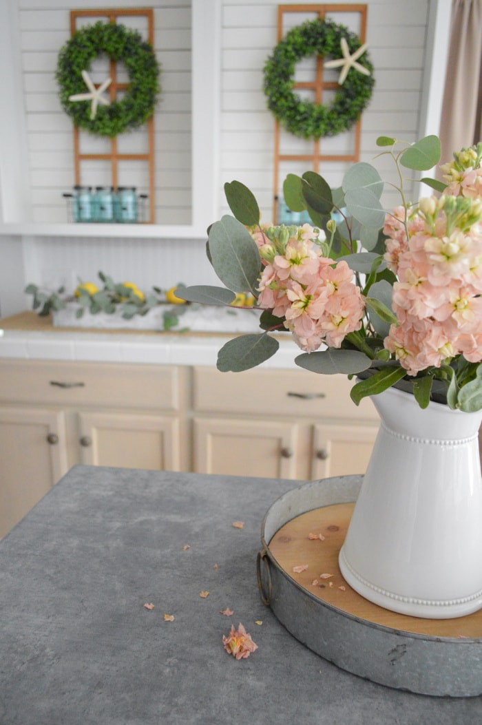 pink flowers in a white vase with eucalyptus in front of kitchen wall with farmhouse decor