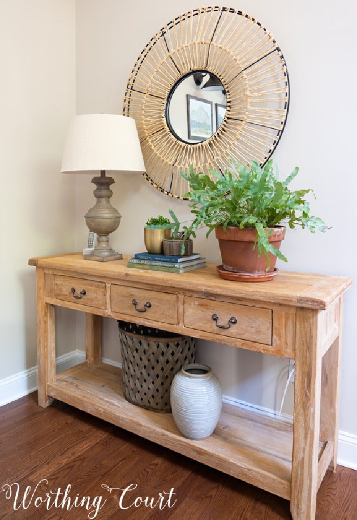 wood console table topped with a lamp, accessories and a plant and a round mirror on the wall above