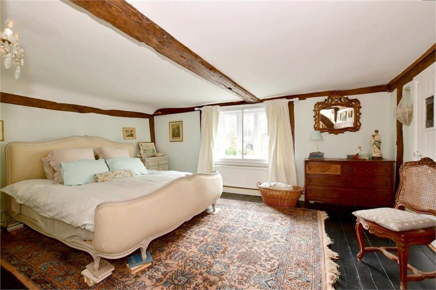 bedroom of English cottage home with large white bed and exposed wooden beams