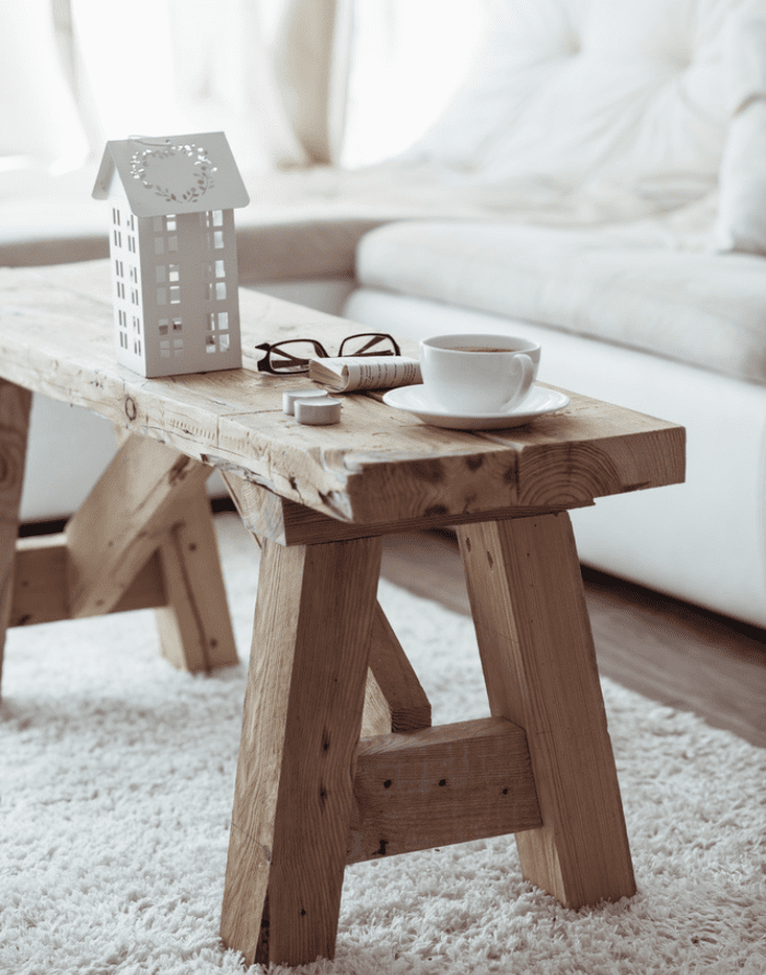 raw wood bench with a coffee cup against an ivory sofa