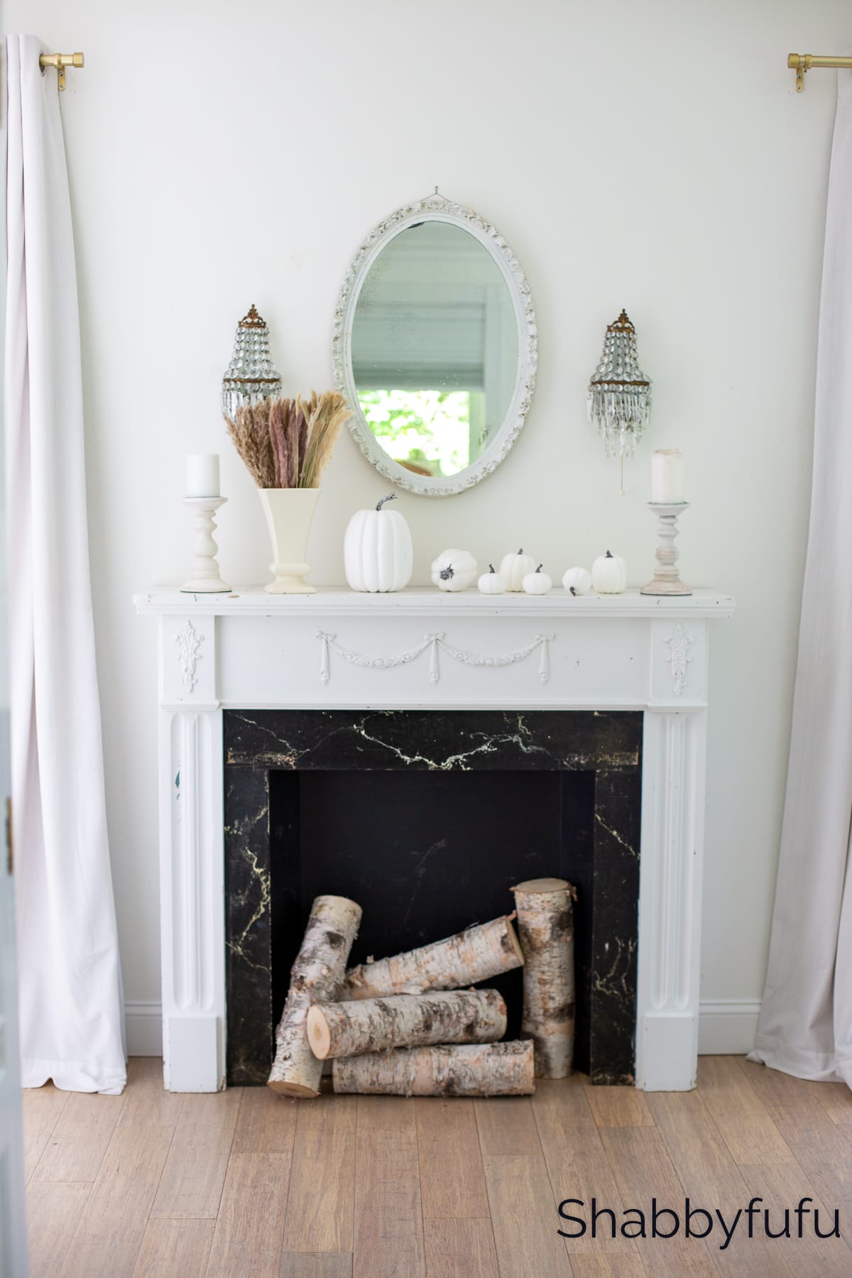 fireplace with white fall themed mantle showcasing white pumpkins, candleholders, shabby chic mirror and wood logs 
