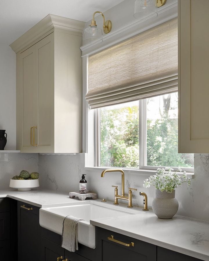 A kitchen with a large window featuring linen romen curtains as the window treatments.