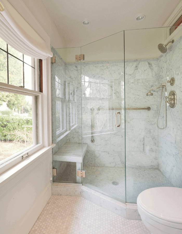 A bathroom with a large window featuring Roman shades as the window treatments.