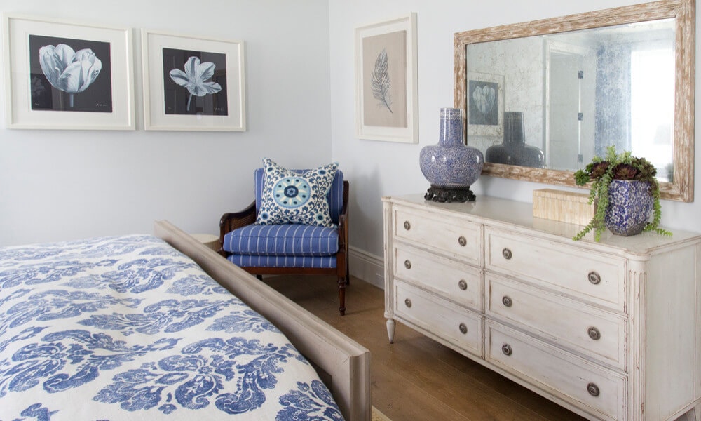 bedroom in a cozy coastal home featuring white and blue bedding and farmhouse distressed inspired furniture