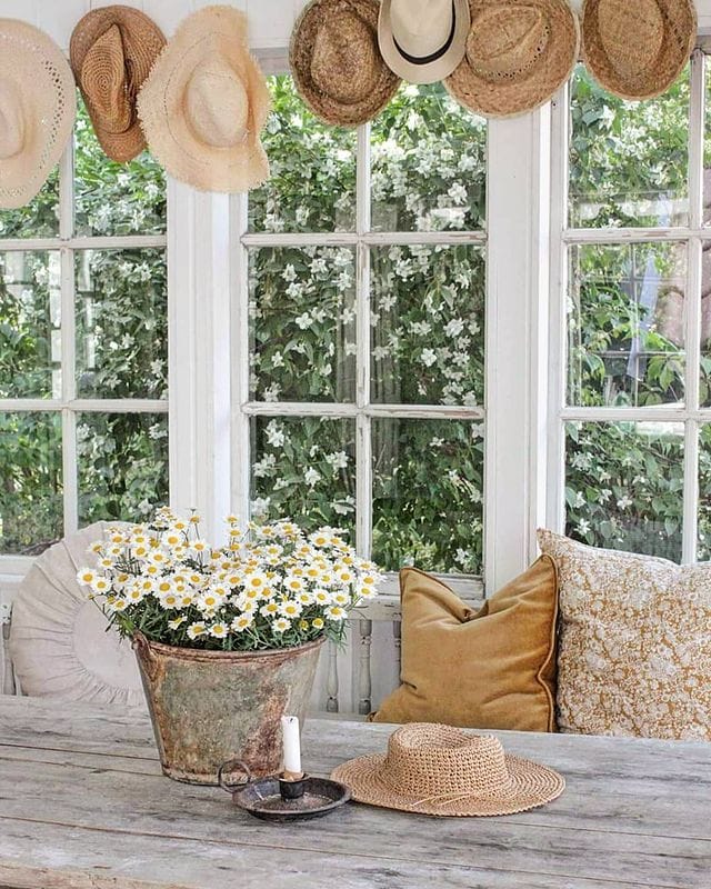 summery cottage style dining room featuring yellow pillows, tustic dining table and floral arrangements