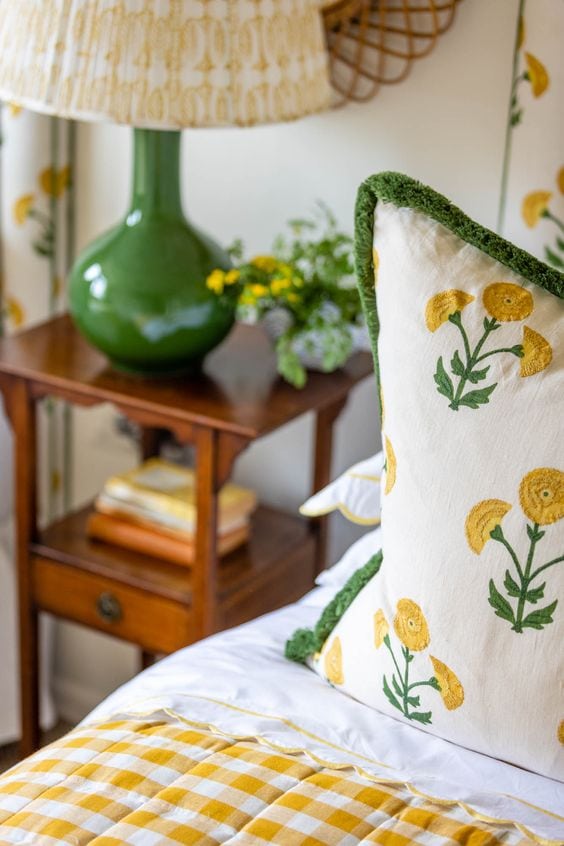 closeup image of bed featuring pillows in white and yellow floral patterns and checkered duvet, from a cottage