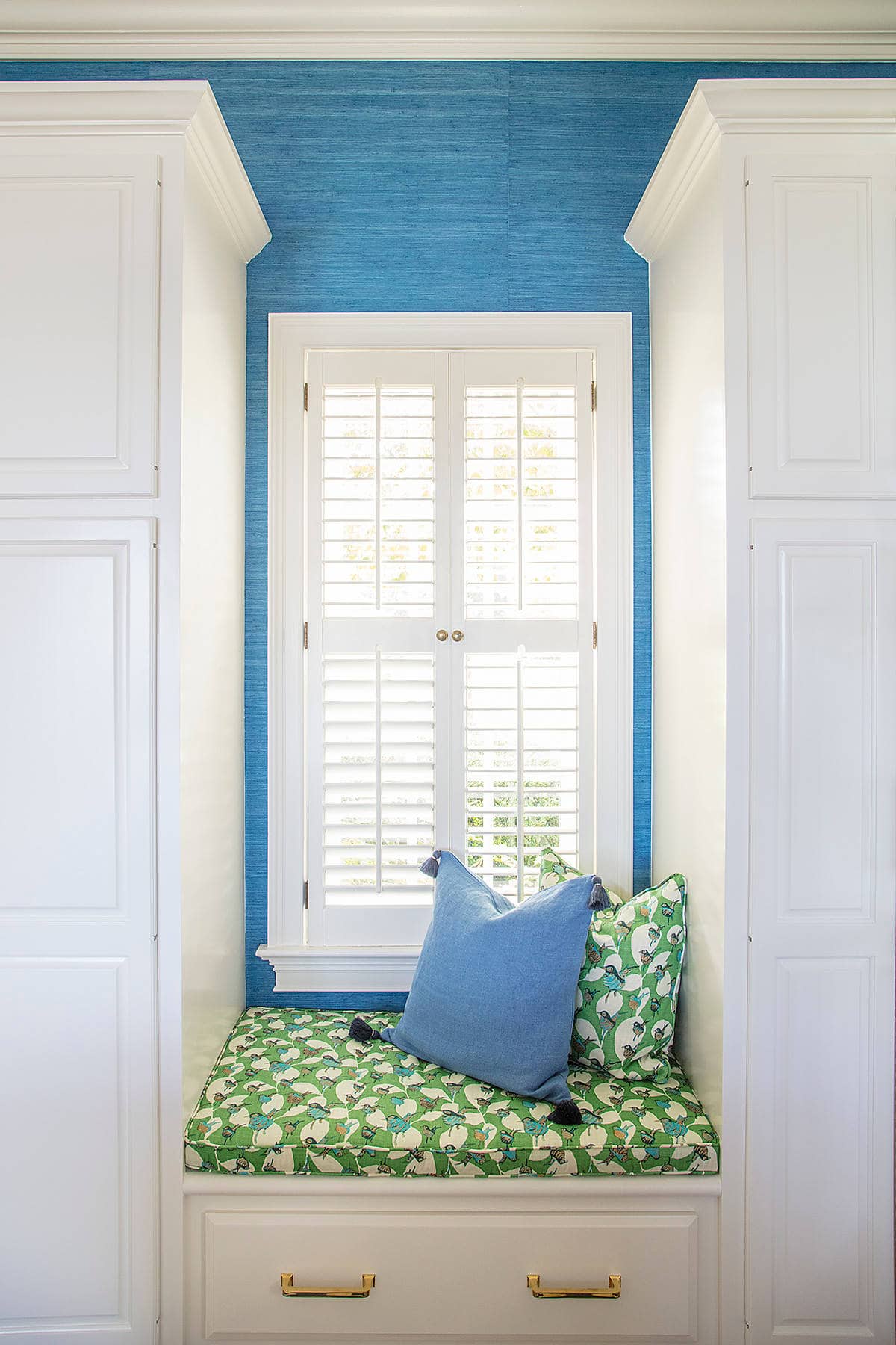 Home Tour: Window nook featuring a white window, blue wall and built-in seat with green patterned pillow