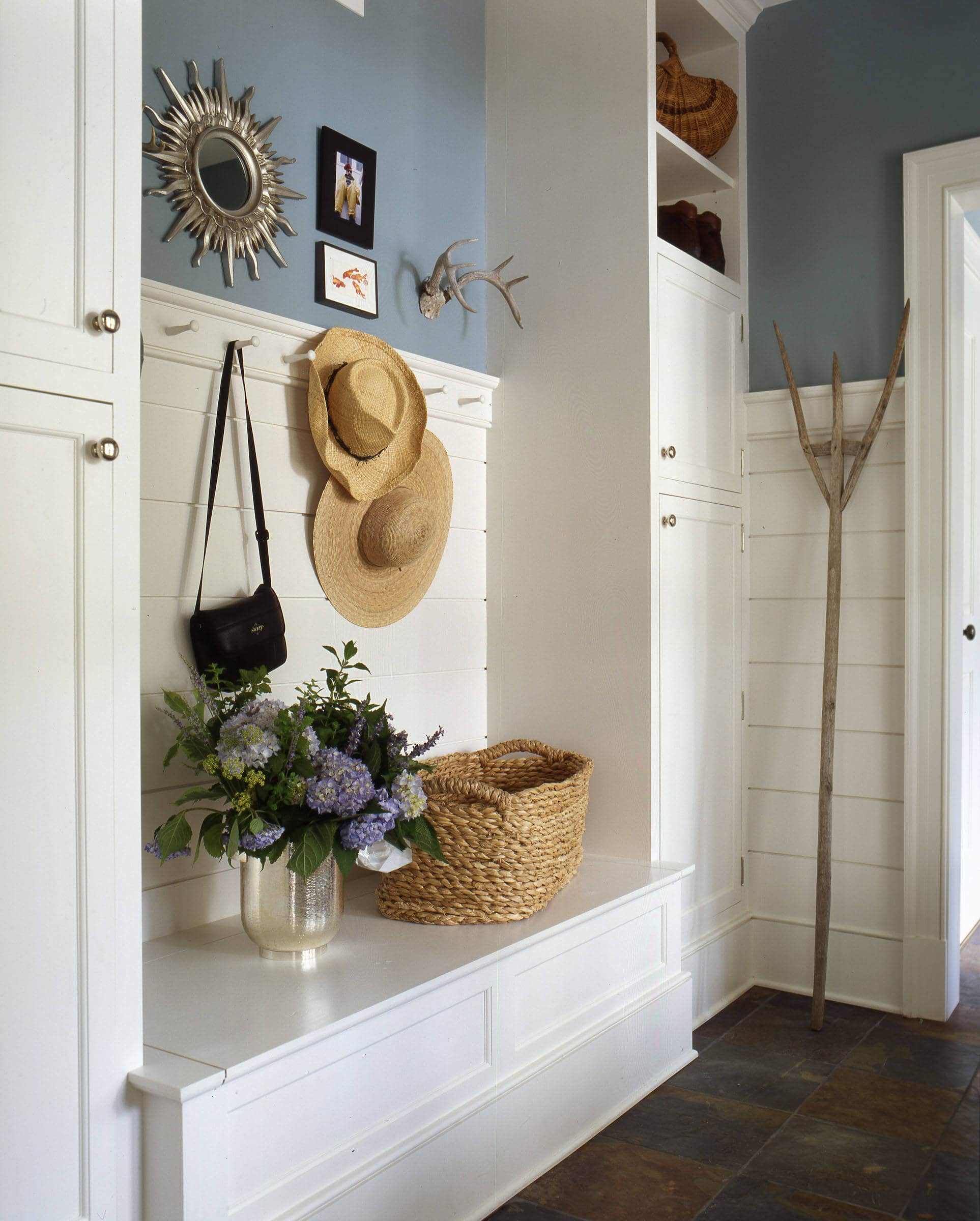 Dark wood floor entryway featuring a mudroom cabinets, light blue wall and hats hanging from hooks, photo for entryway ideas