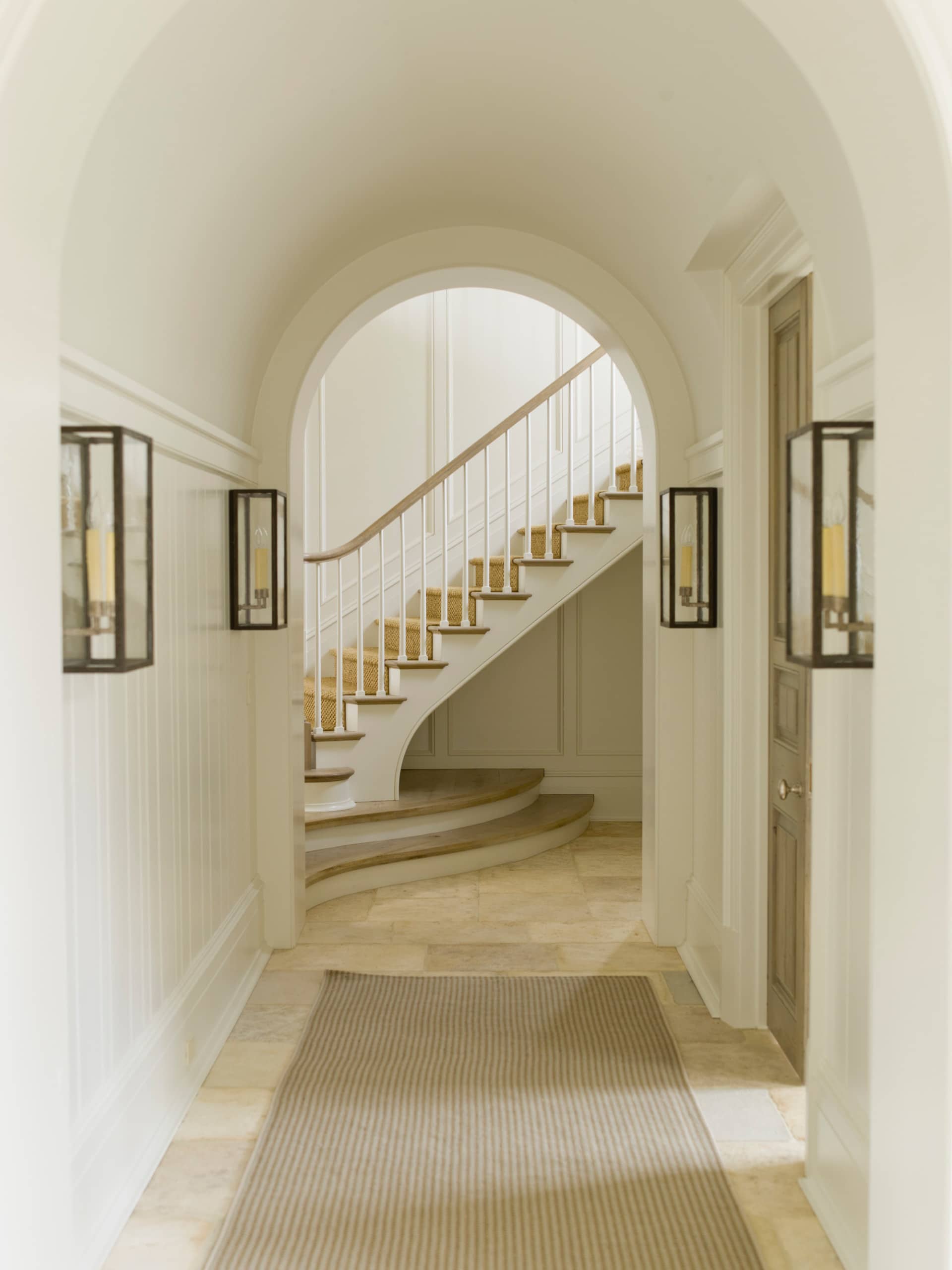 Traditional hallway in home tour featuring an arched threshold with a staircase in the back