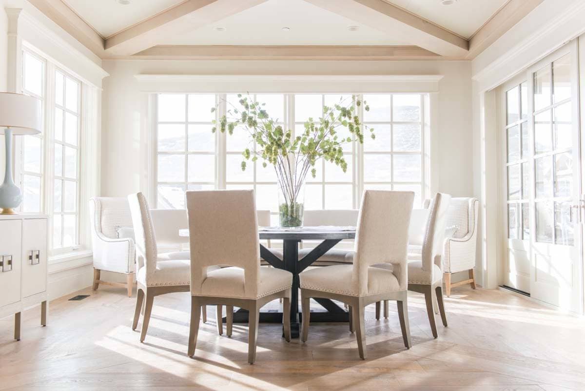 European style home tour dining room featuring large windows, round black table and beige chairs