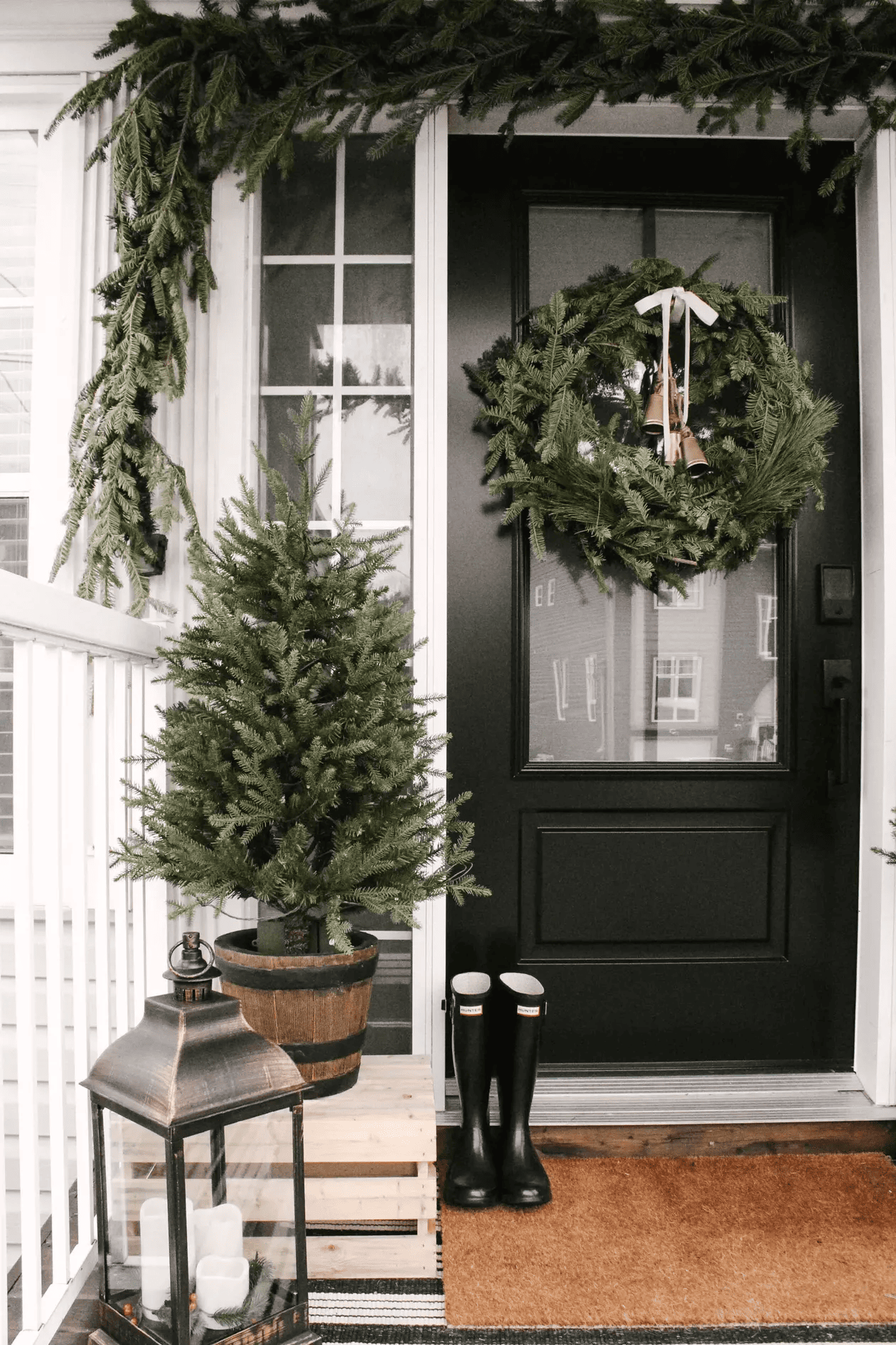 Black front door with green wreath and Christmas trees featuring outdoor decorating ideas