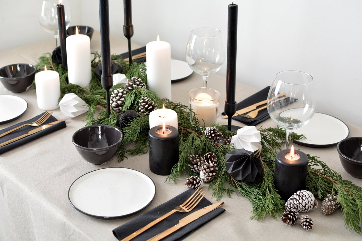 Simple holiday centerpiece featuring white candles, black candle holders and greenery