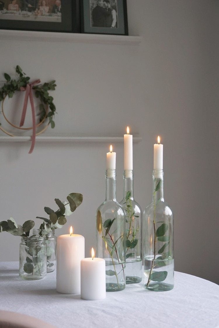 Minimalist idea for a centerpiece featuring white candles onm top of glass bottles