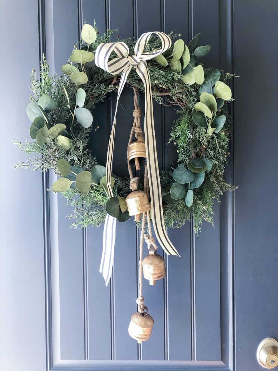 Wreath made of greenery, bells ribbon against a blue front door