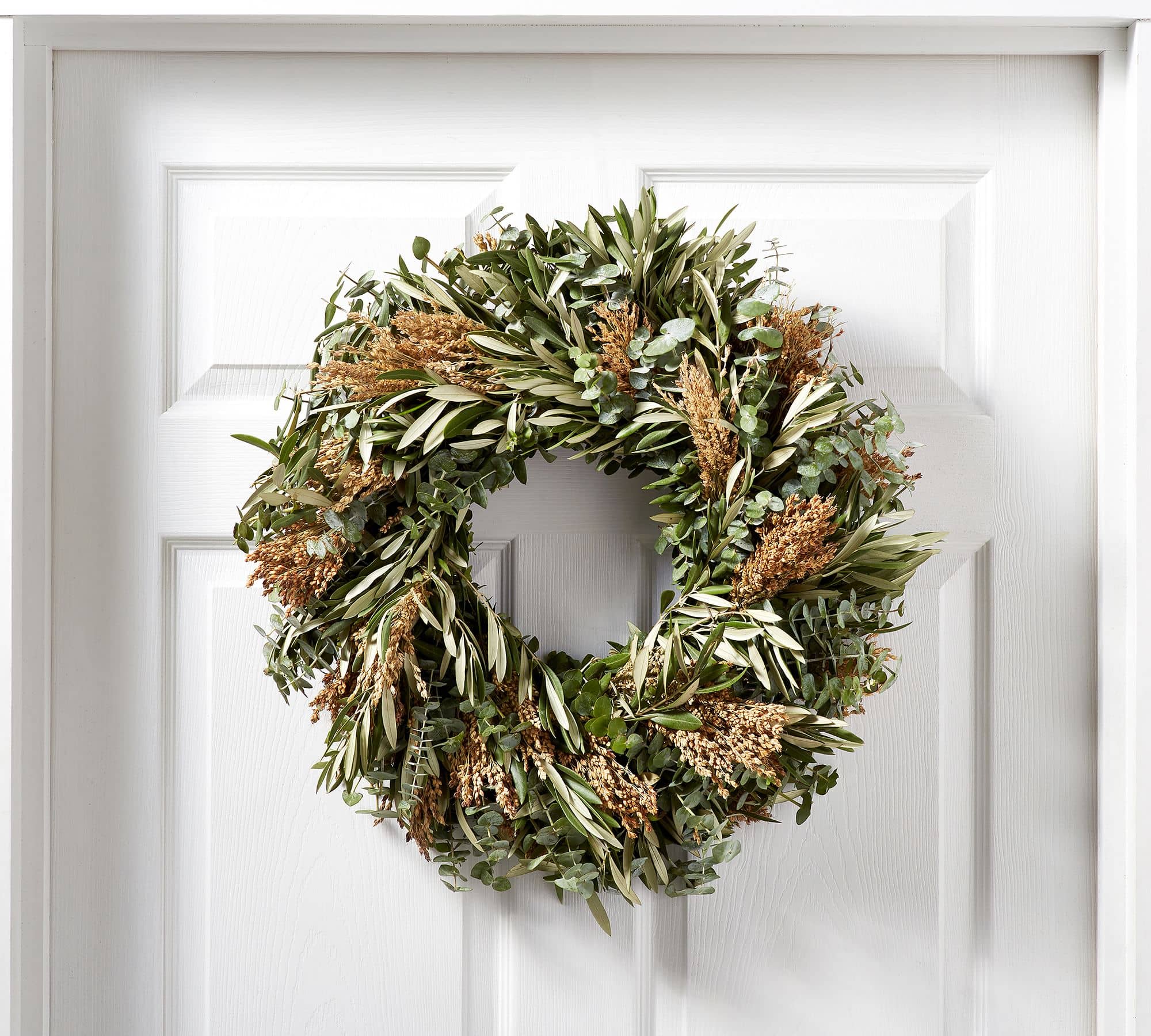 Wreath made of greenery with a bell against a white front door