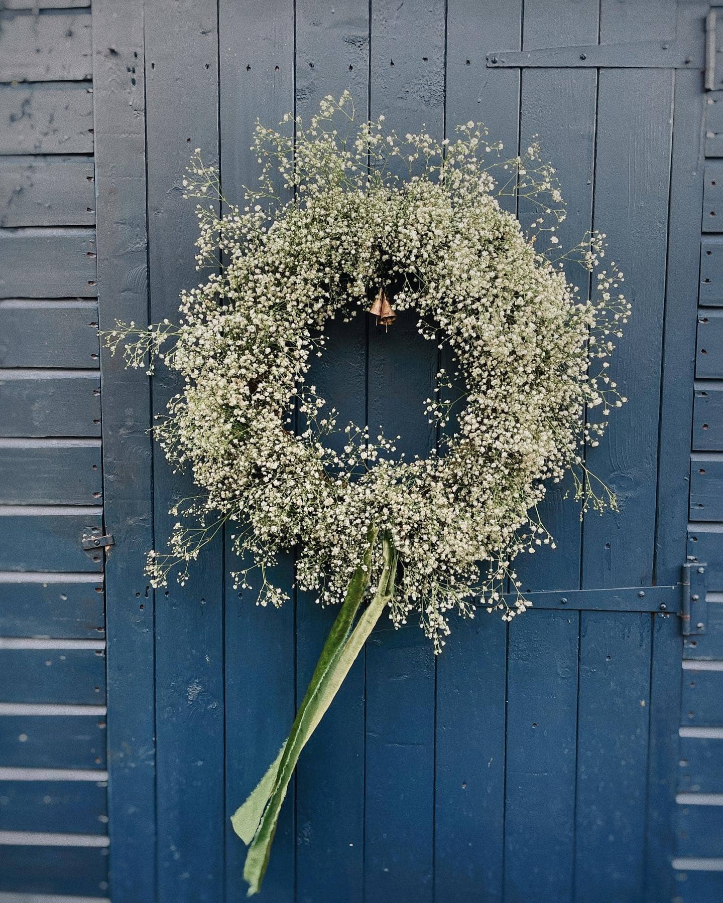 Wreath made of greenery and baby's breath and ribbon against a blue front door