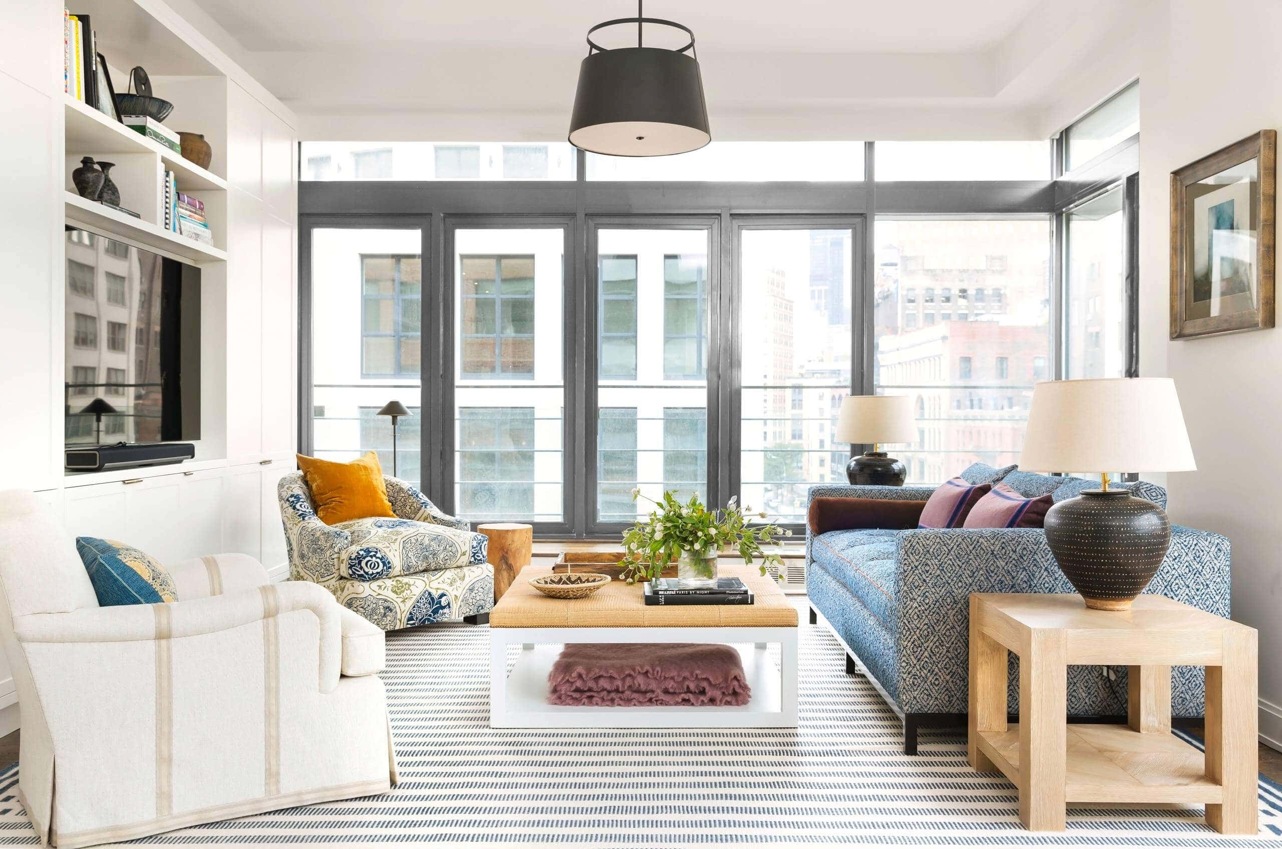 Living room with white walls and floor-to-ceiling windows. White and blue patterned sofa as a focal point, accented by neutral armchairs. Transitional aesthetic with sophisticated ambiance.