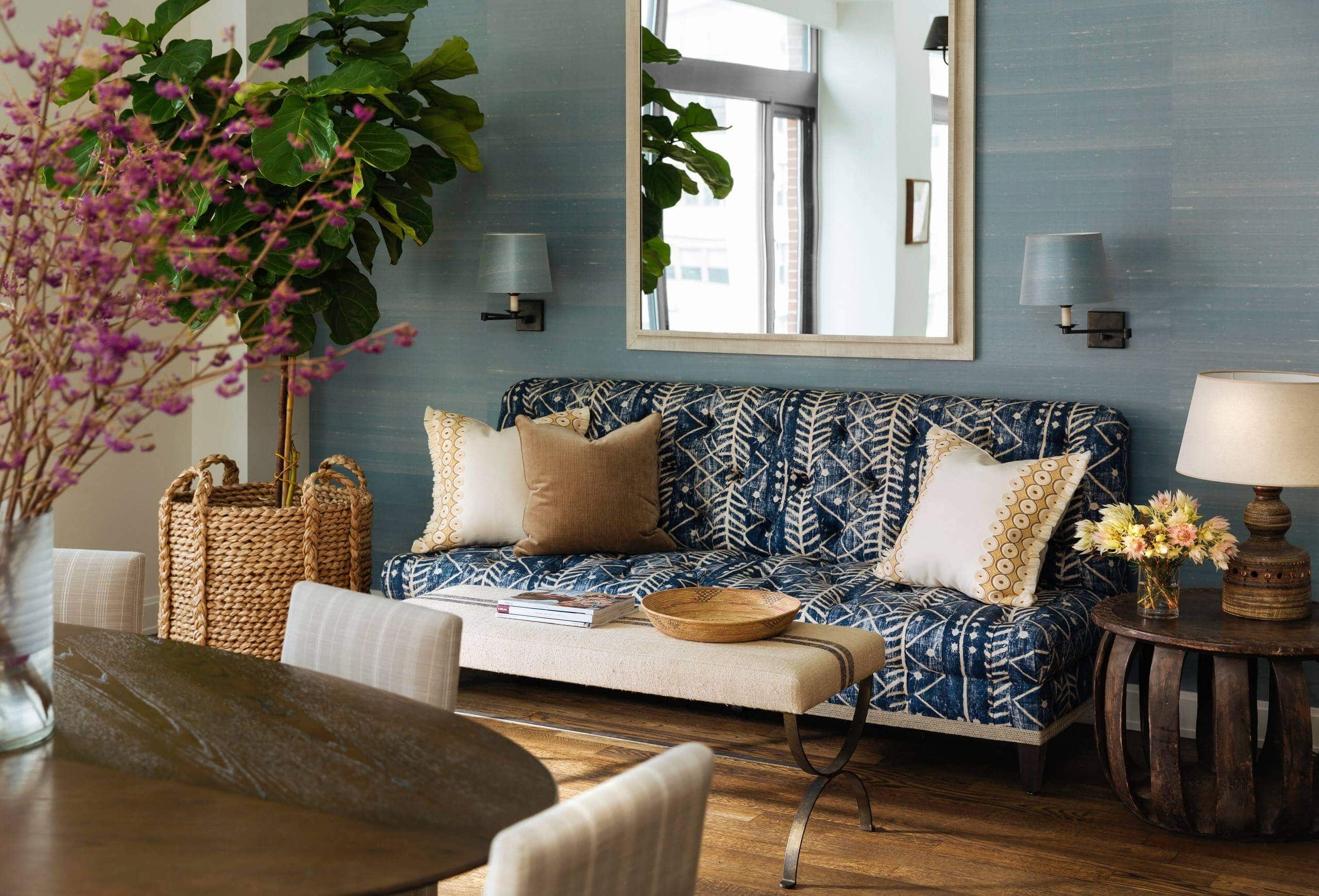 Living room with blue walls and large mirror. White and blue patterned sofa as a focal point, accented by mustard and white throw pillows. Transitional aesthetic with sophisticated ambiance.