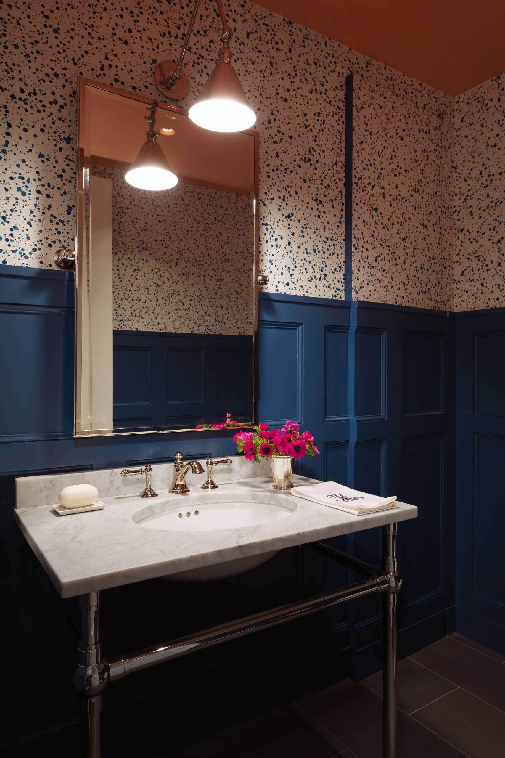 Small and moody powder room featuring a navy wall and patterned wallpaper. Transitional aesthetic with chic ambiance.