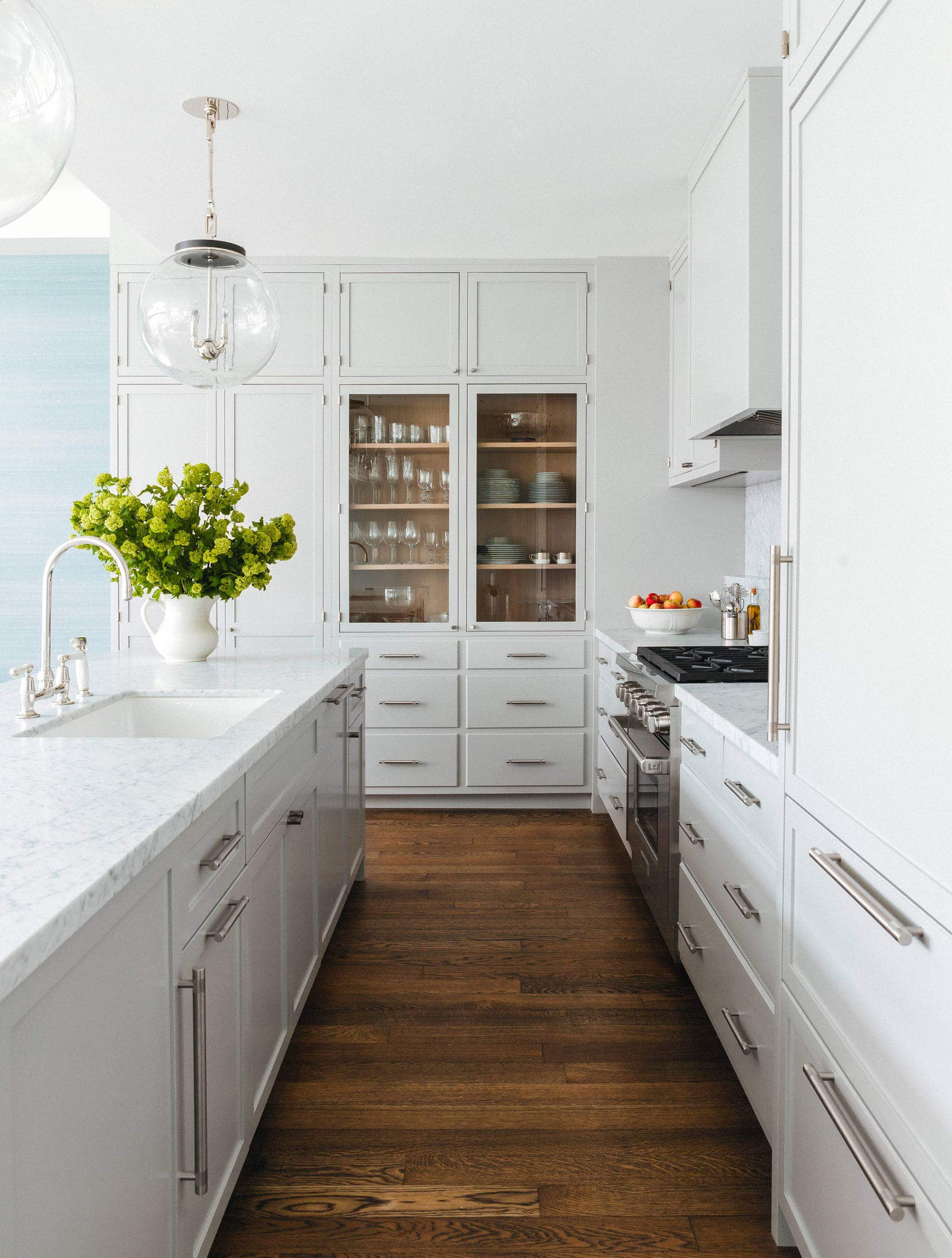 Kitchen with white walls and marble countertops. Light grey built-in crockery cabinet as a focal point, accented by a large kitchen island. Transitional aesthetic with sophisticated ambiance.