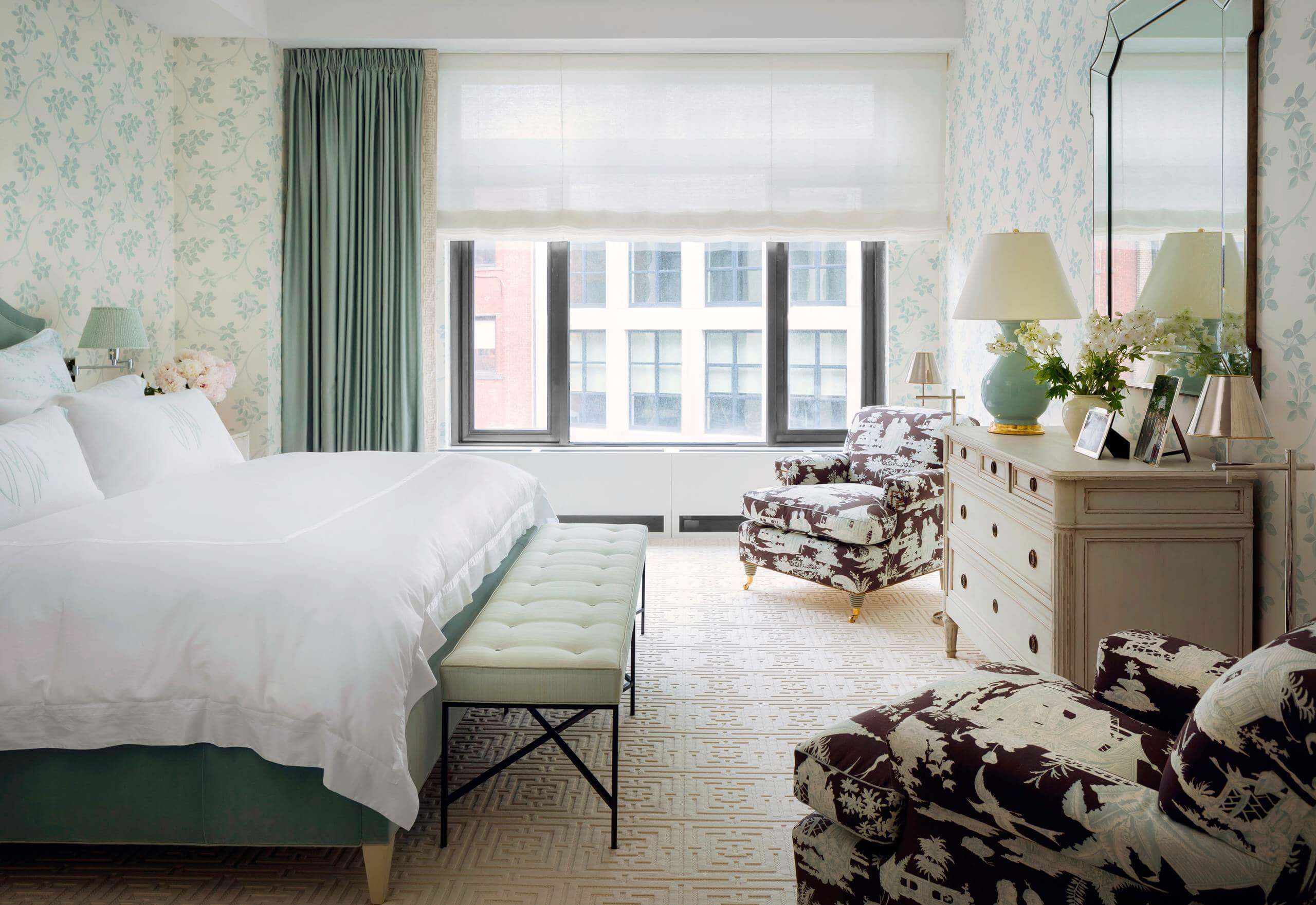 Chic bedroom with serene aqua walls. Large bed and ivory rugs work as the focal points, accented by a patterned armchair. Transitional aesthetic with sophisticated ambiance.