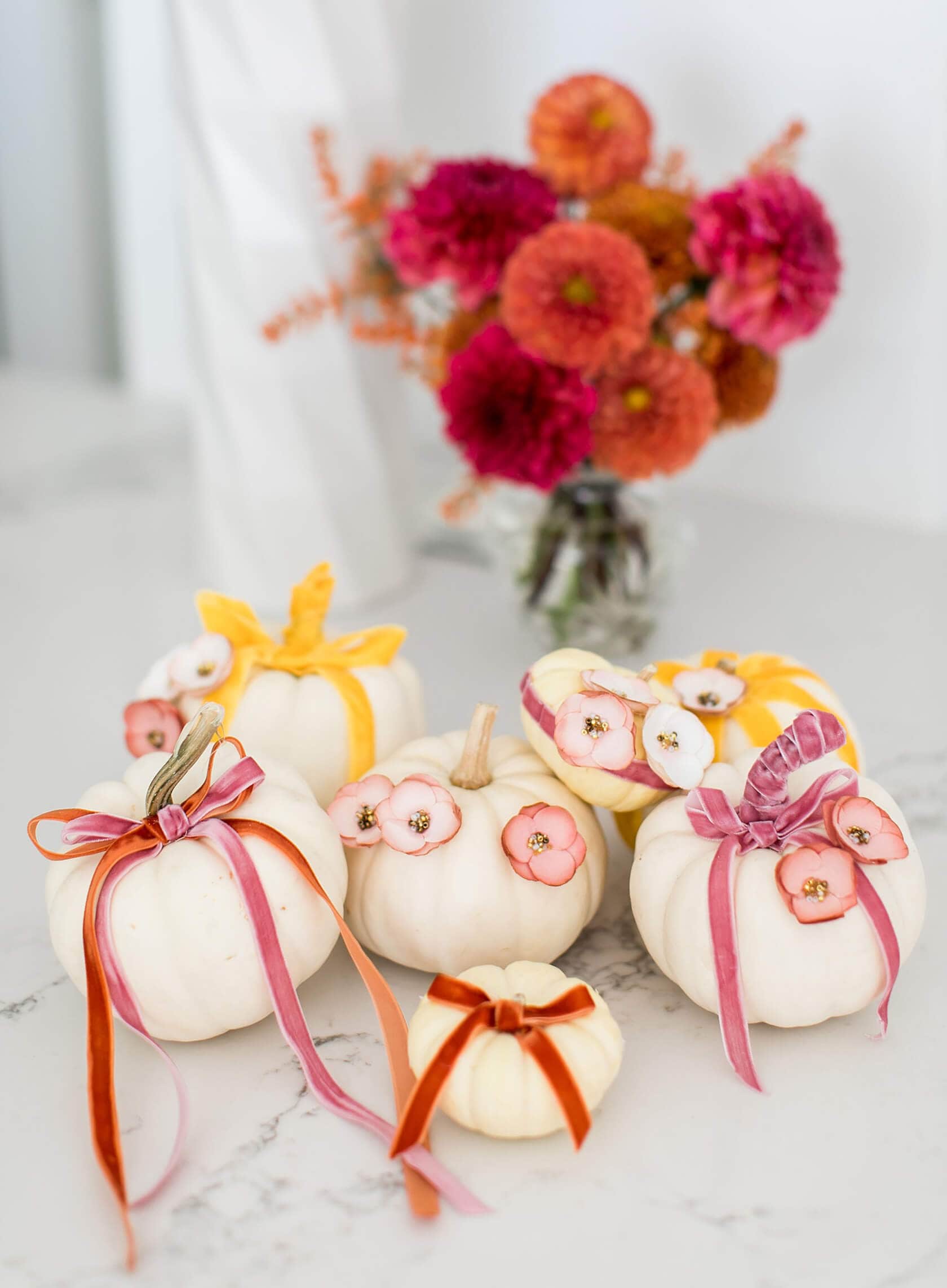 Creative no carve pumpkin decorating idea featuring ivory pumpkins with flowers and ribbons in red, pink and yellow