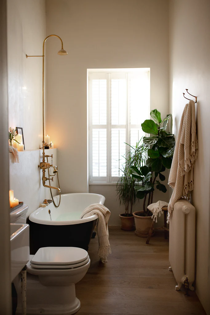 Fall bathroom decor idea featuring cozy bathtub with lit candles and plants