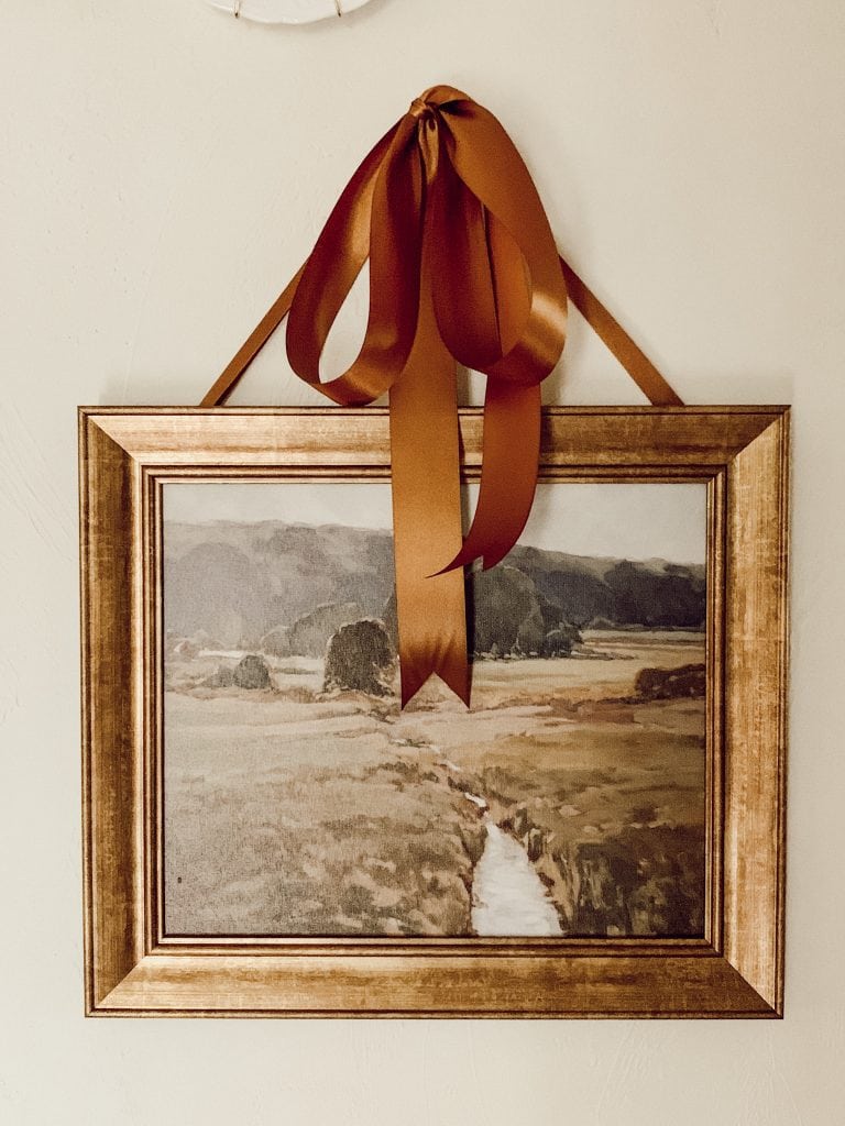 Example of minimalist fall decor ideas featuring a autumn inspired landscape with a velvet bow hanging above