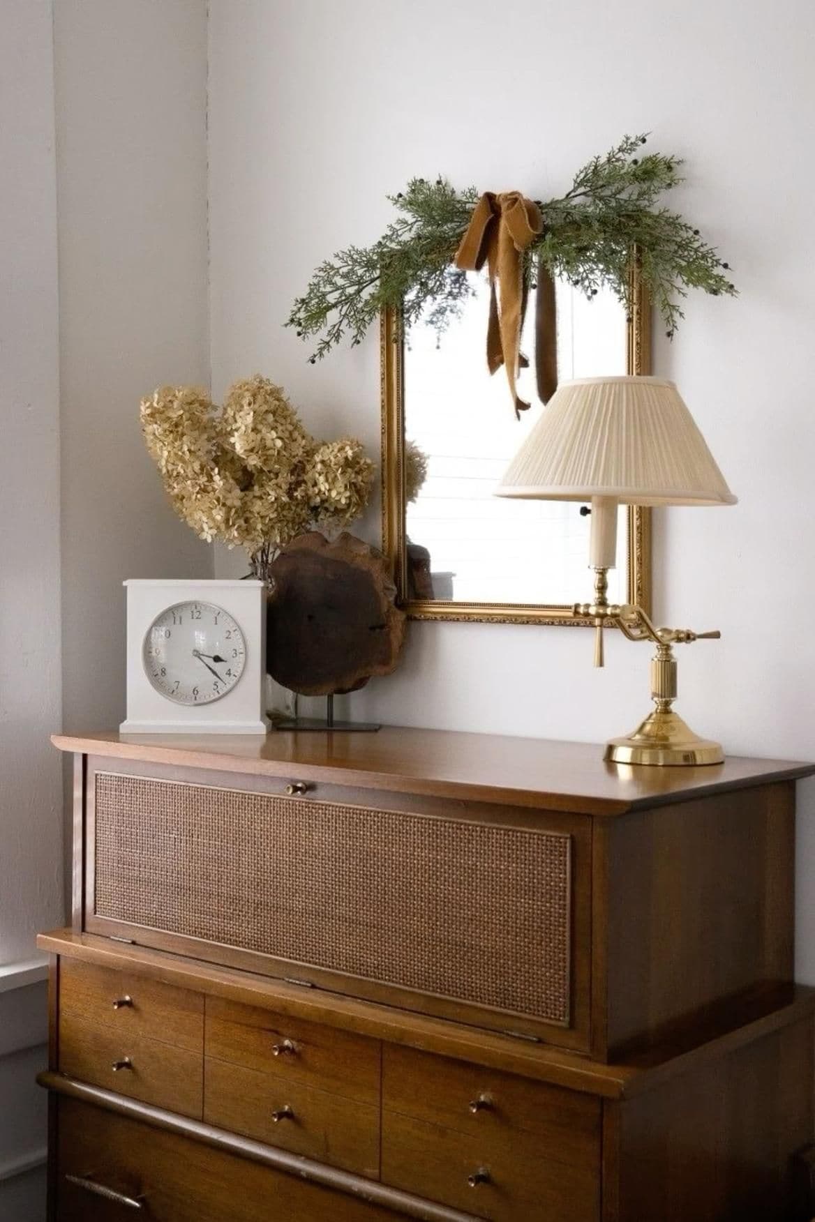 Example of minimalist fall decor ideas featuring a console tale entryway with a mirror framed by greenery and velvet bow