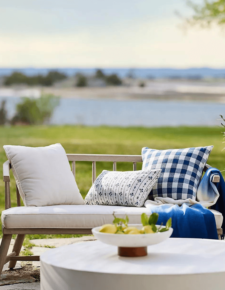 Close up of patio furniture inspo featuring modern wicker sofa with white and blue patterned pillows