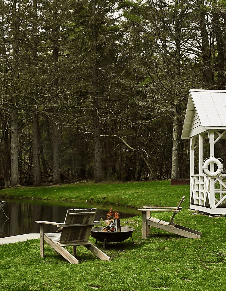 Close up of patio furniture inspo featuring outdoor chairs next to a fire pit looking at a lake