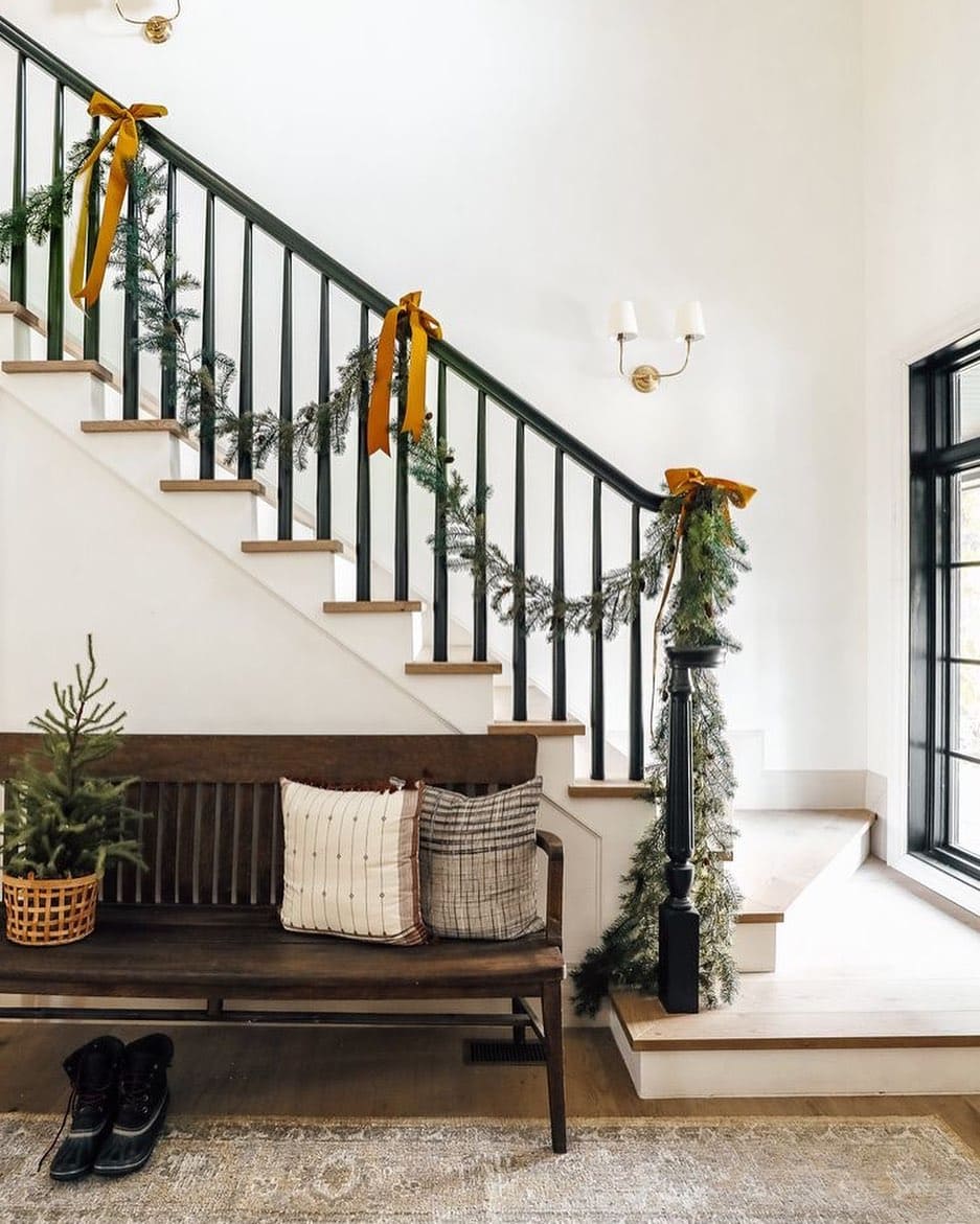 Christmas staircase decor idea featuring a modern staircase with dark yellow bow with green garland.