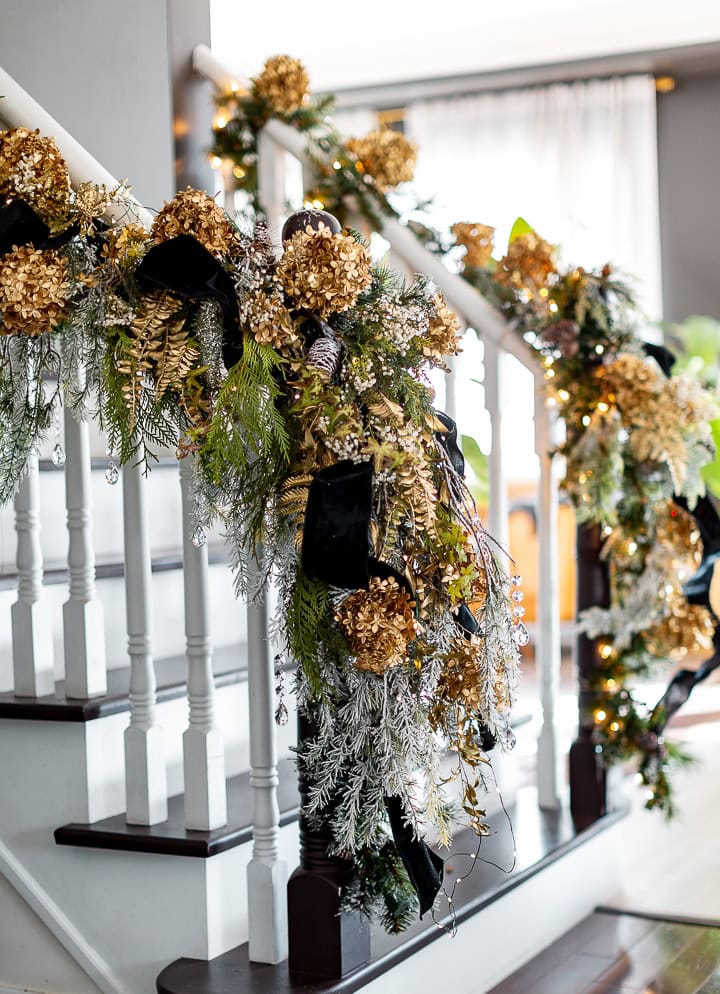 Christmas staircase decor idea featuring a traditional entrance in gold, and silver with black ribbons and green garland.