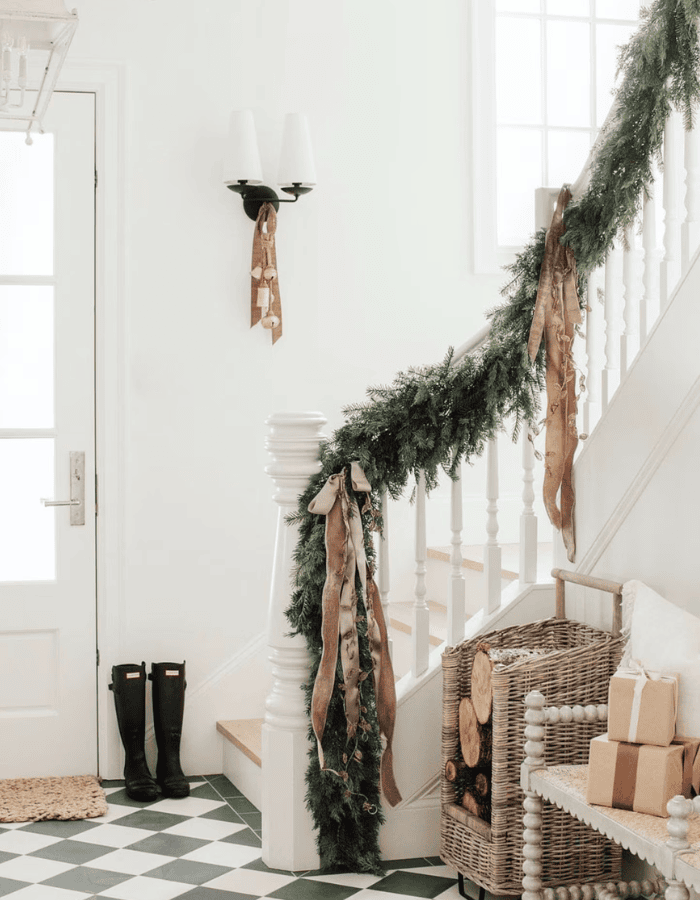 Christmas staircase decor idea featuring a green garland and pale taupe bows.