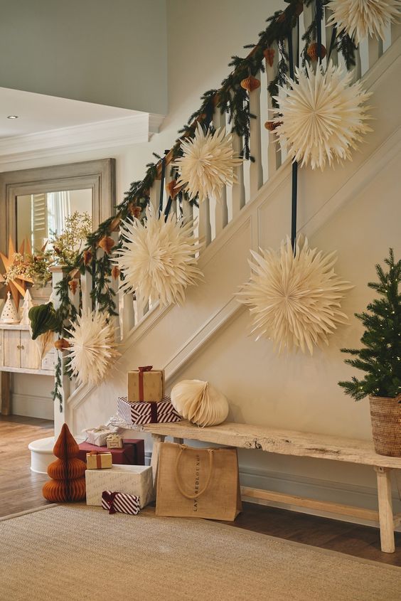 Christmas staircase decor idea featuring a paper stair ornaments hung from green garlands.