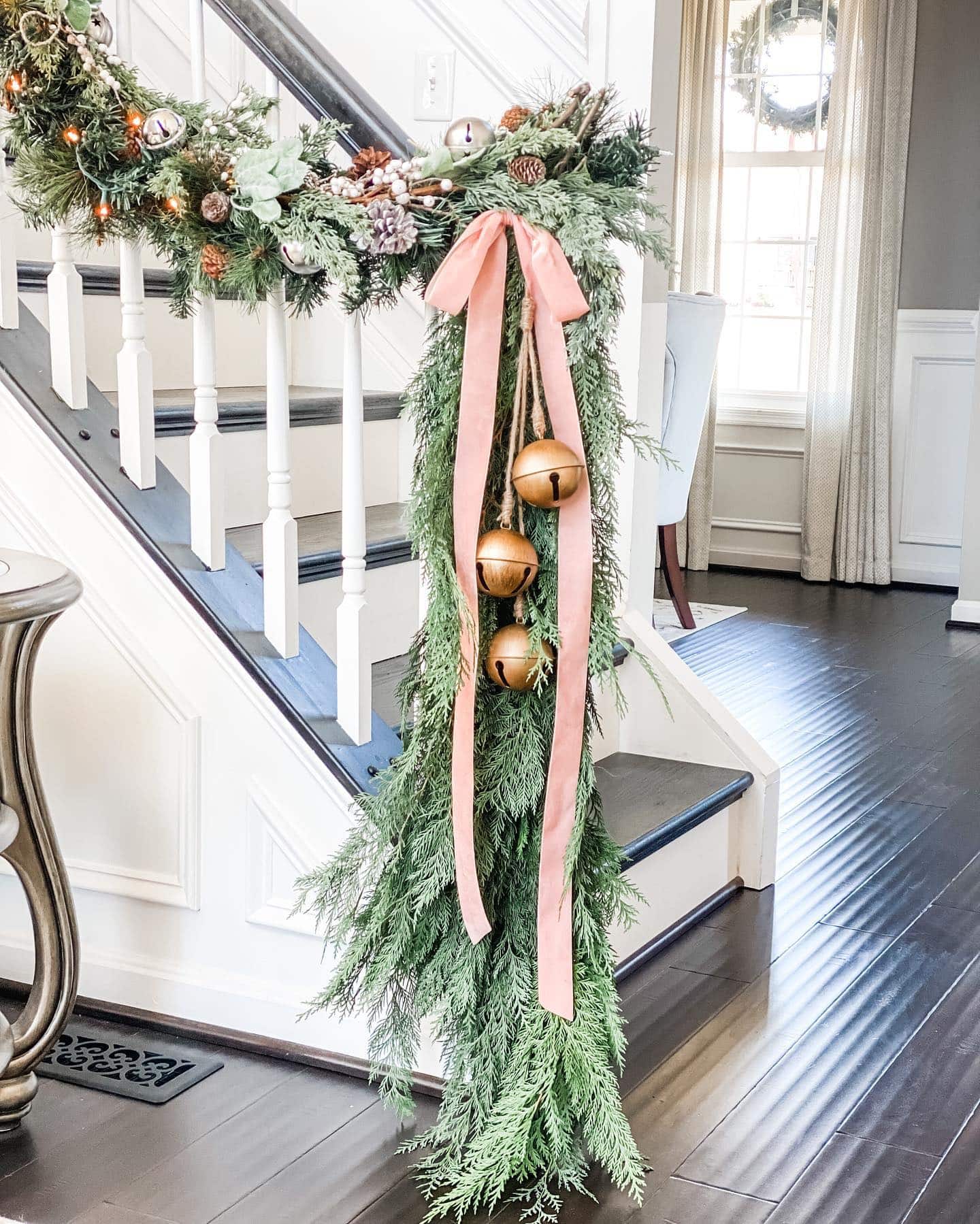 Christmas staircase decor idea featuring a vintage-inspired look with a green garland, pink ribbon, and a bell.