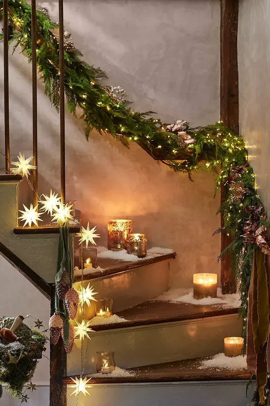 Christmas staircase decor idea featuring a cozy staircase look iwith star shaped candles and pre-lit garlands.