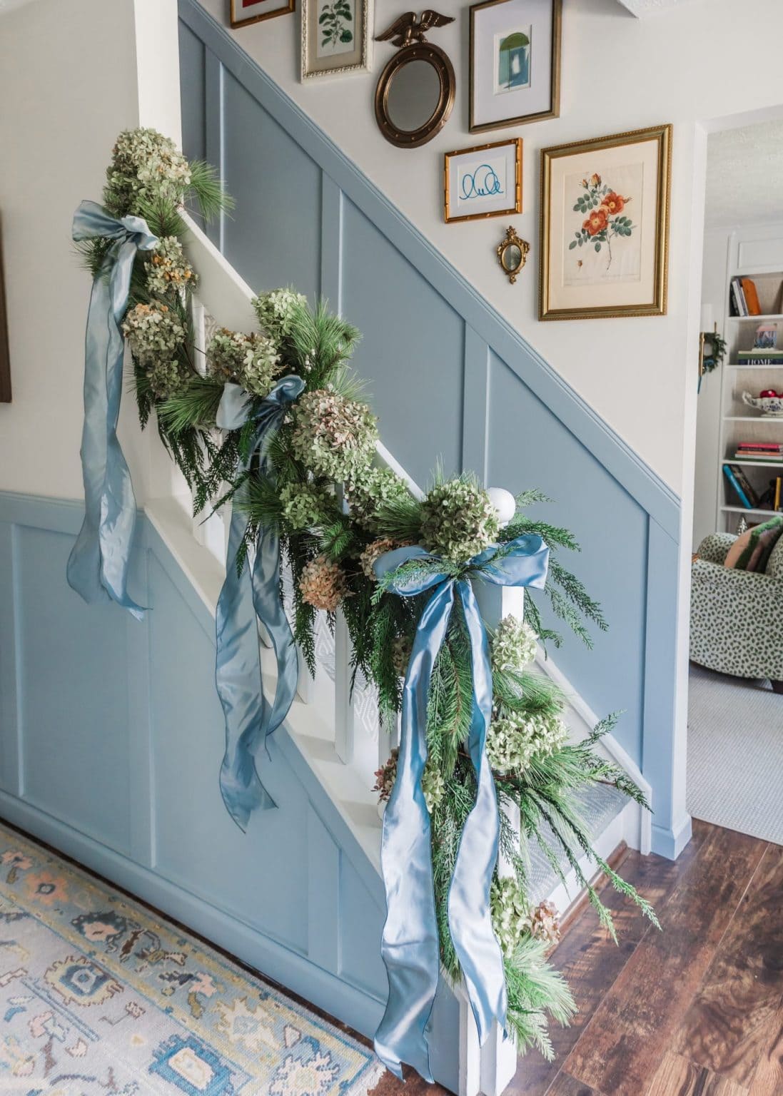 Christmas staircase decor idea featuring a traditional entrance in blue, with light blue ribbons with green garland.